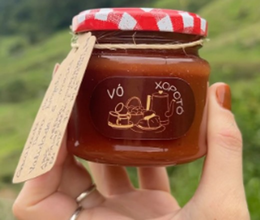 Pote de doce da marca Vó Xopotó, com etiqueta artesanal, sendo segurado na mão